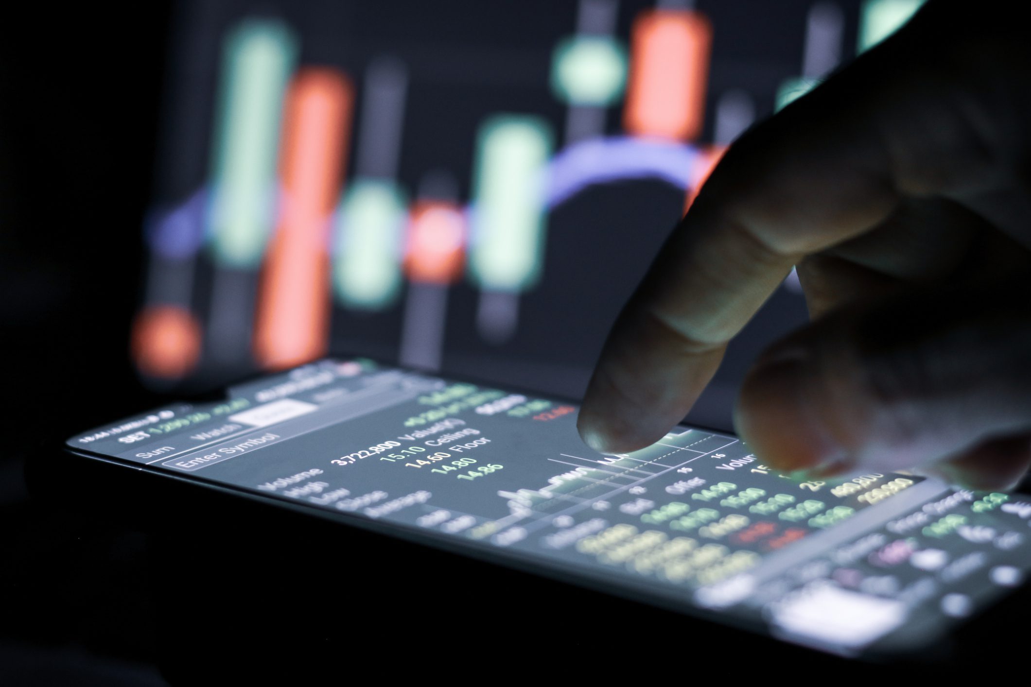 Finger touching financial graph on smartphone screen.