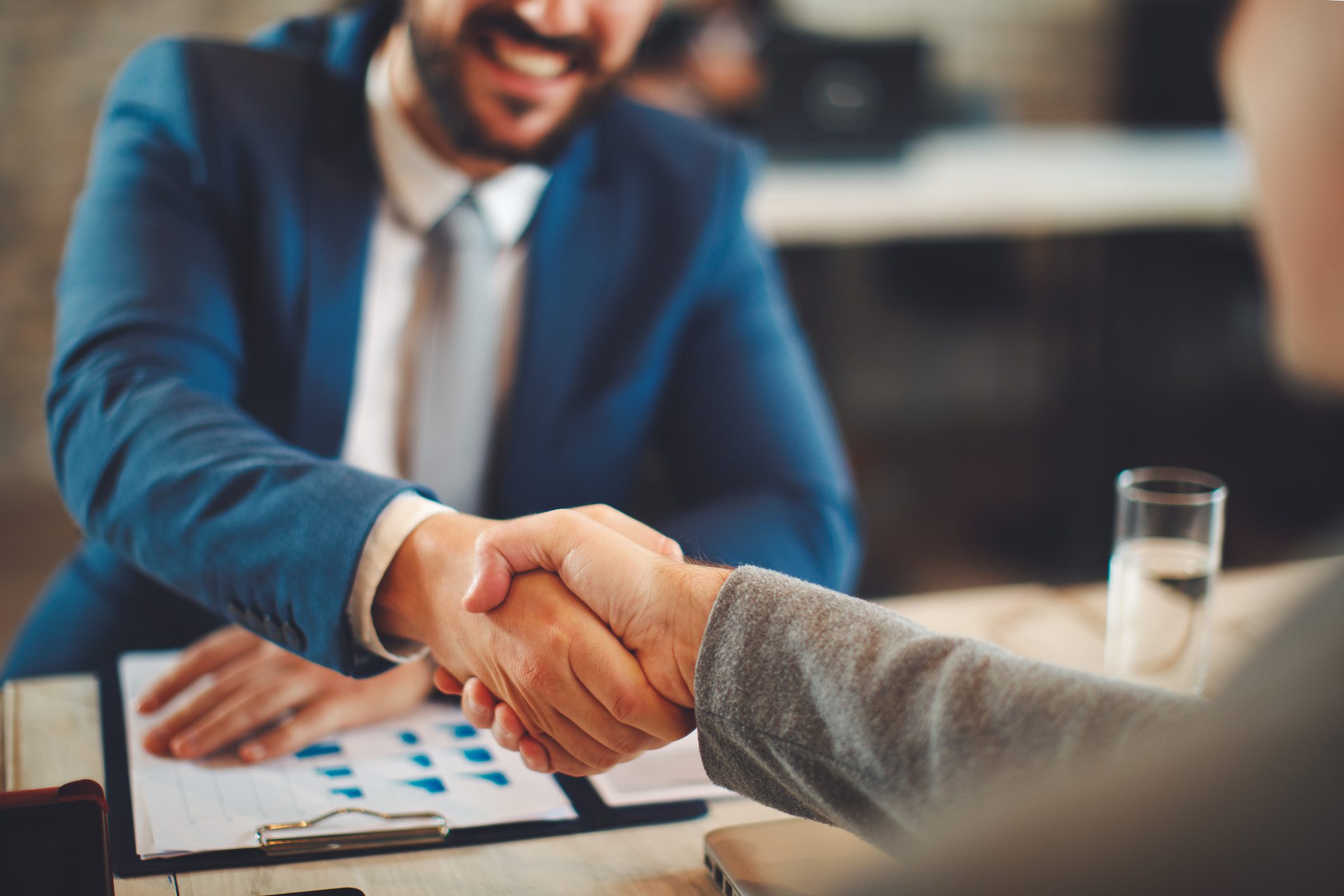 Two people shaking hands across table.