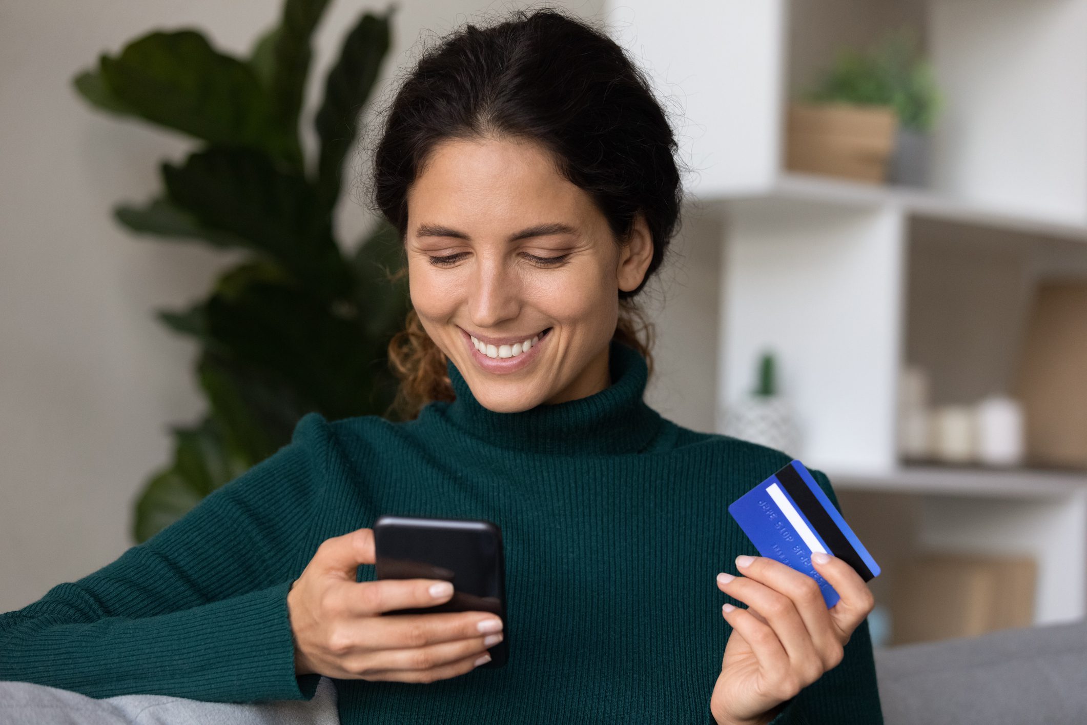 Woman smiling using phone and holding card.