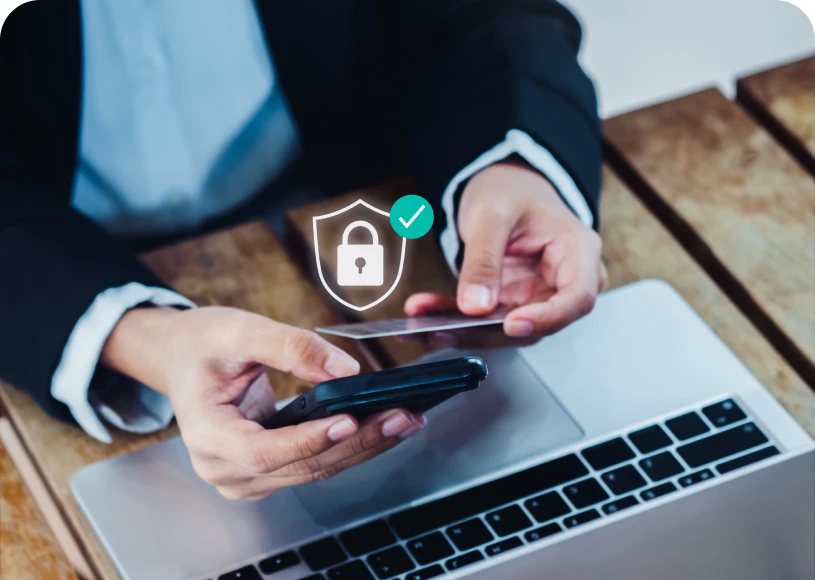 Hands with phone, laptop, security icon displayed.